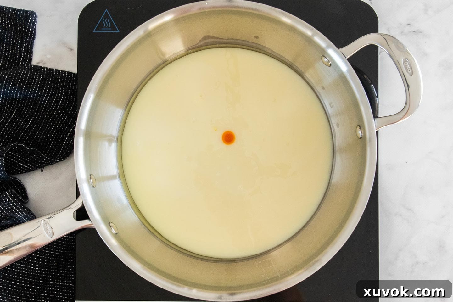 Condensed milk, lemon extract, and a small dot of yellow food coloring swirled together in a saucepan, ready for heating.