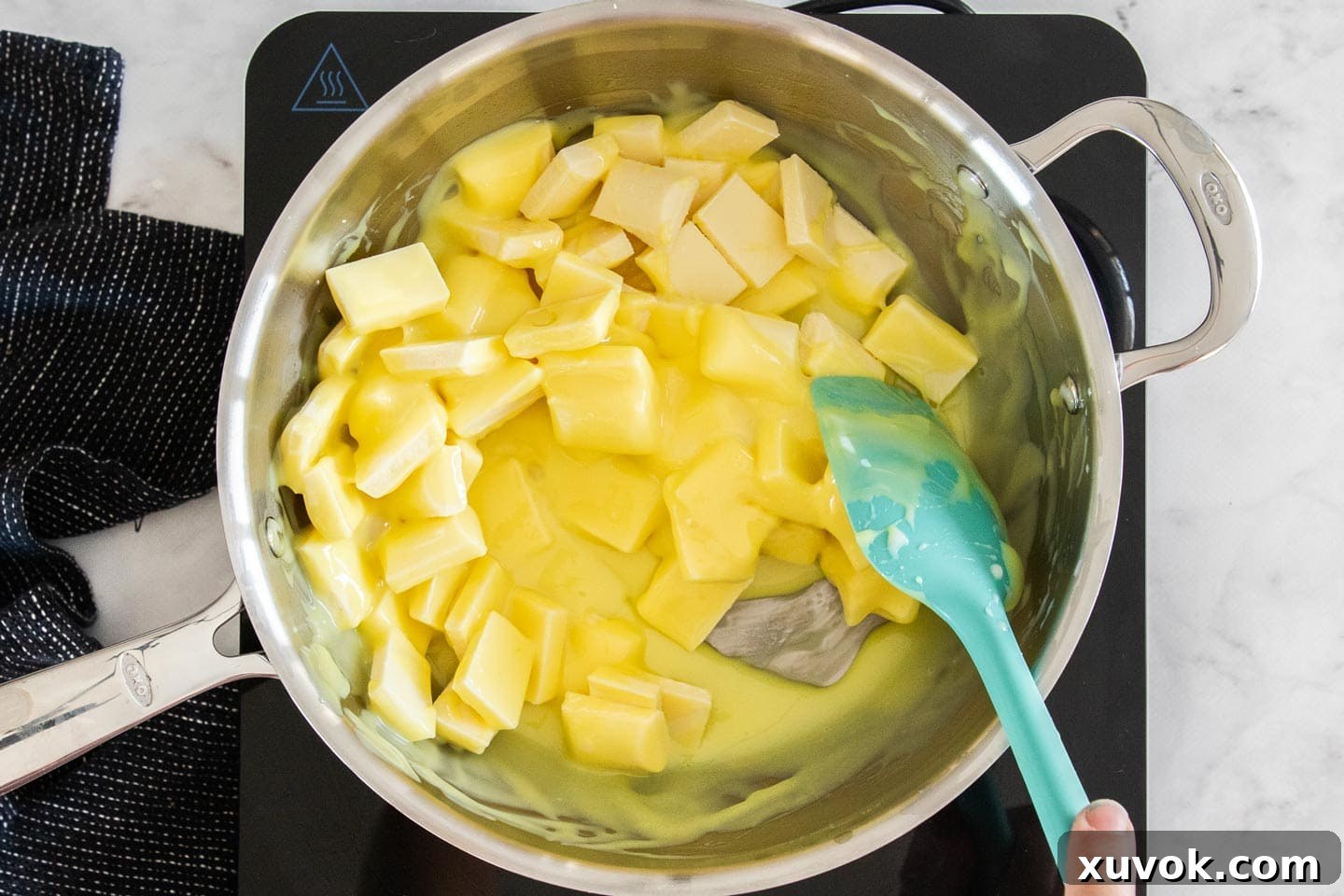 The white chocolate slowly melting and blending into the condensed milk mixture in a saucepan, creating a smooth, creamy texture.