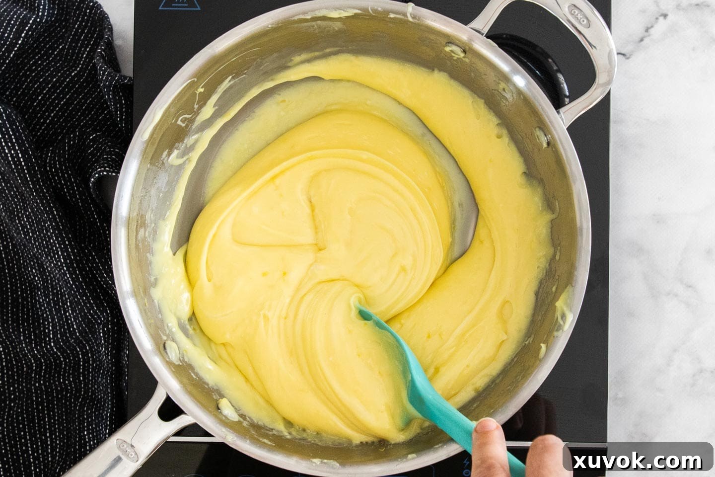 Finely grated lemon zest being stirred into the smooth, yellow lemon fudge mixture in the saucepan.