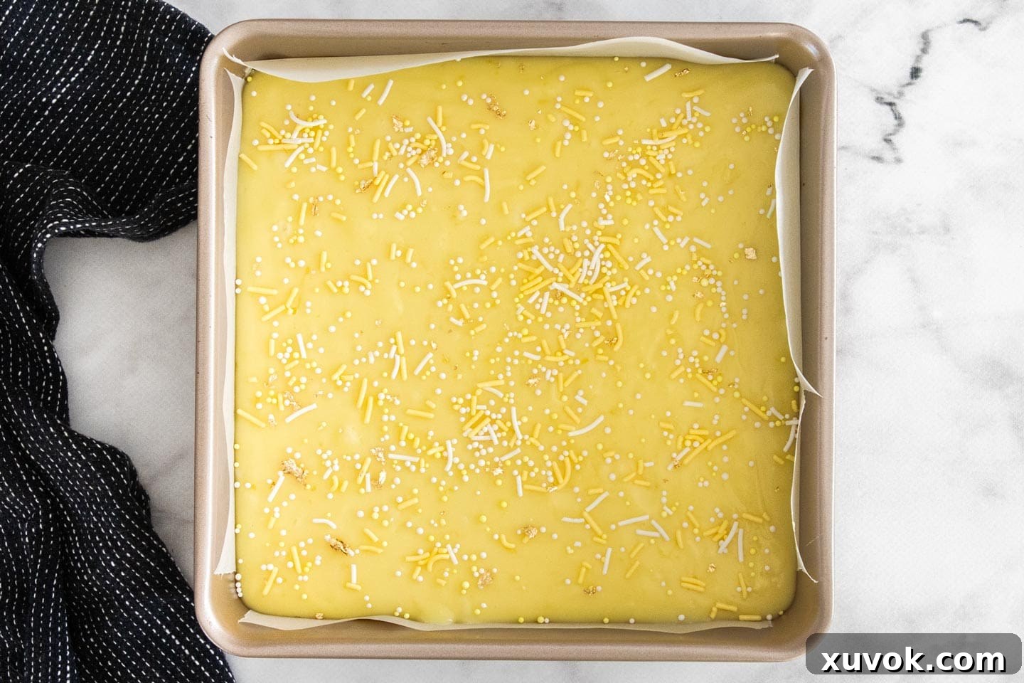 The lemon fudge mixture in a square baking pan, topped with colorful sprinkles and ready for chilling.