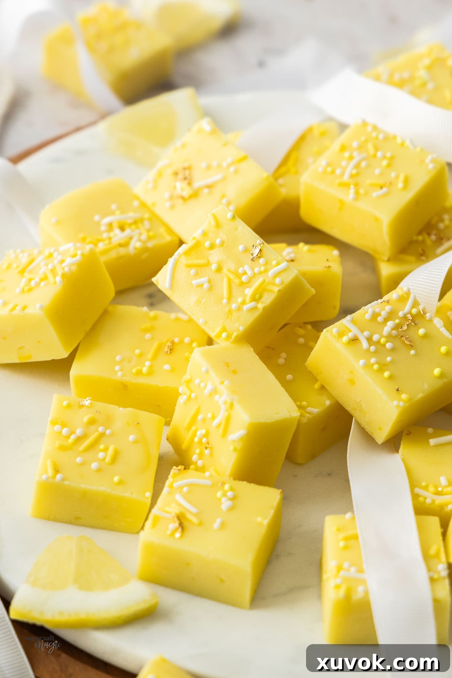 Many squares of vibrant yellow lemon fudge piled neatly against each other on a white serving platter, ready to be enjoyed.