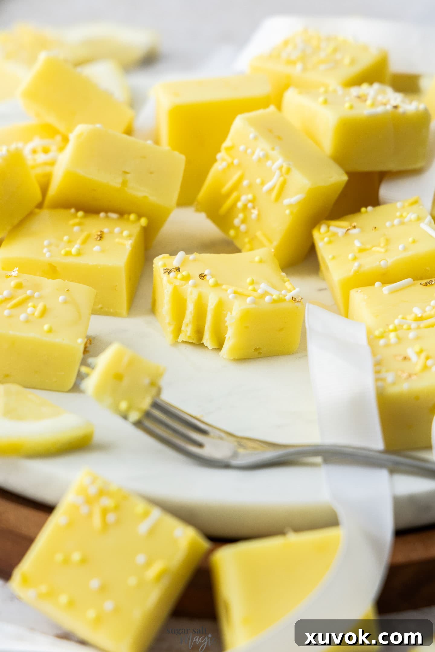 A perfectly cut square of lemon fudge with a bite taken out by a fork, showcasing its creamy interior.