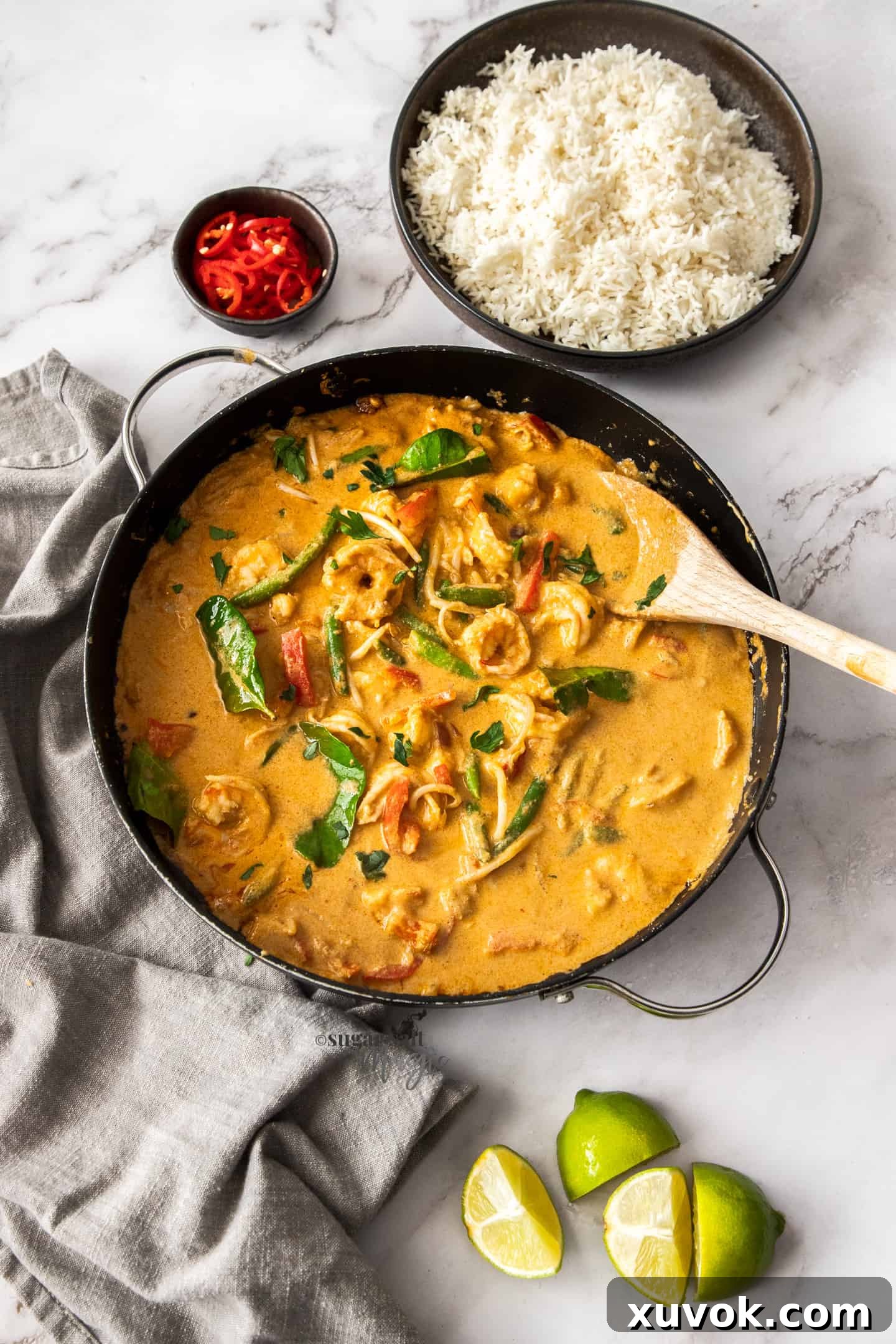 Top down view of a black skillet filled with prawn curry and a bowl filled with rice.