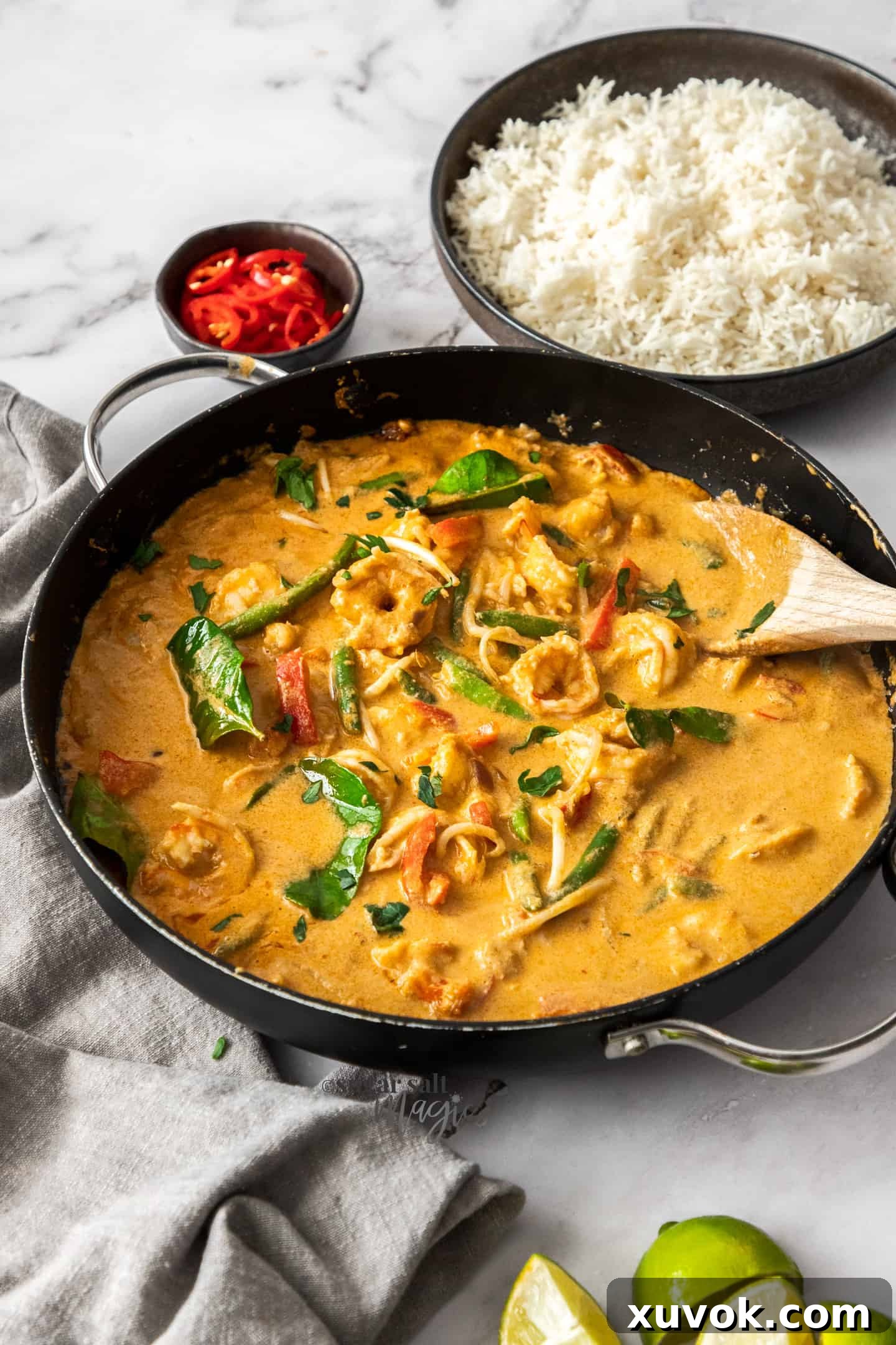 A black skillet filled with prawn curry and a dish of rice in the background.