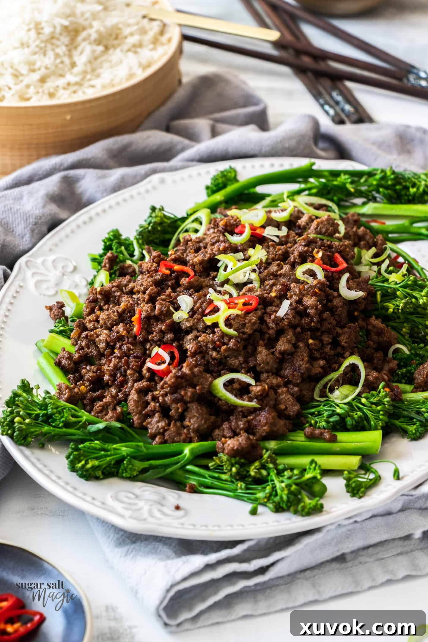 A white plate topped with steamed broccolini and a generous serving of cooked crispy Asian chilli beef mince (ground beef).