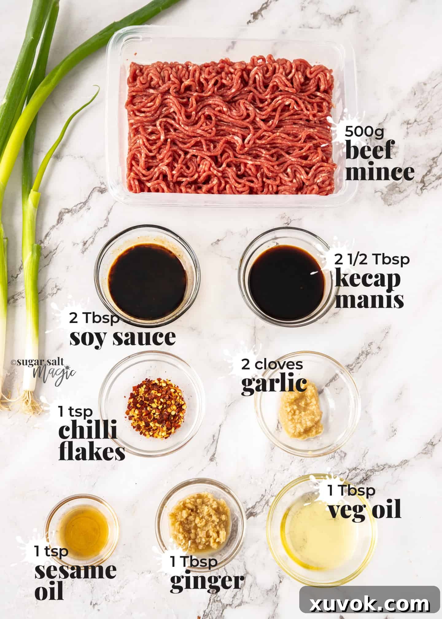 A flat lay of fresh ingredients for Asian chilli beef mince (ground beef) arranged on a white marble worktop, including ginger, garlic, chili flakes, soy sauce, and a bowl of ground beef.