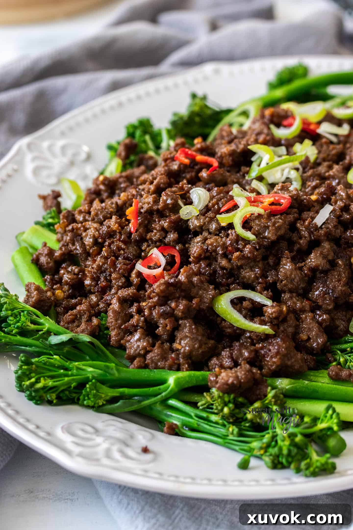 A white plate adorned with a vibrant side of broccolini and a generous helping of perfectly cooked crispy Asian chilli beef mince (ground beef), ready to be enjoyed.