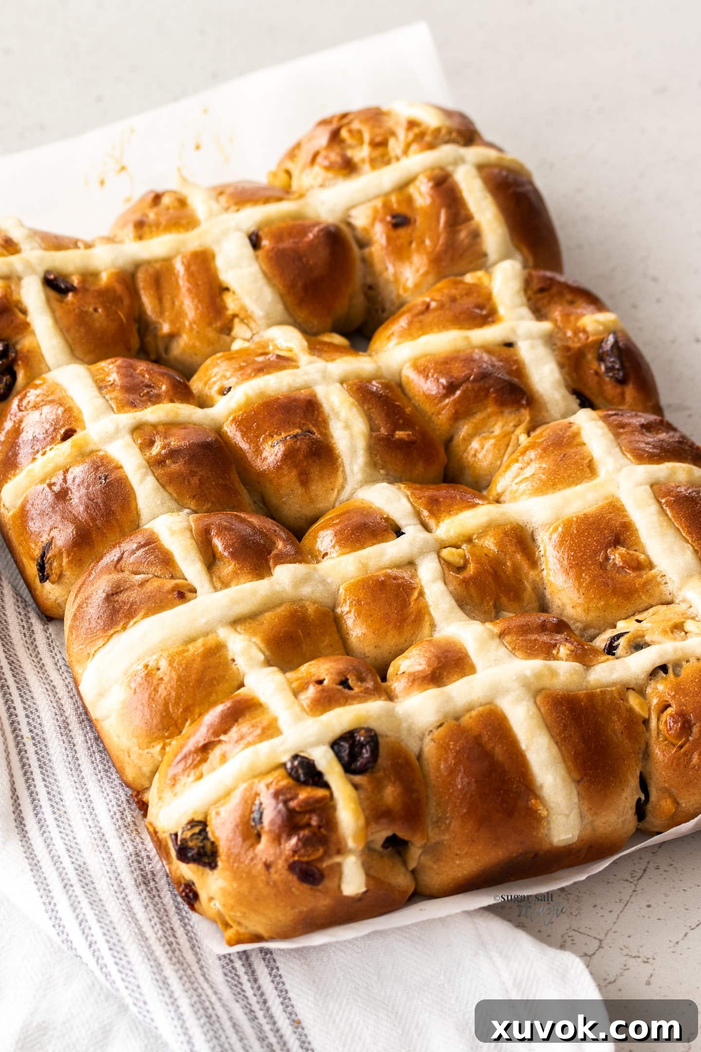 A batch of 12 freshly baked Cranberry White Chocolate Hot Cross Buns, golden brown and perfectly risen, cooling on a rack.