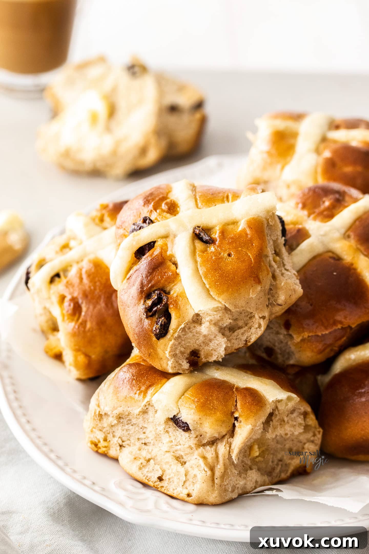 A beautifully arranged plate filled with several golden-brown Cranberry White Chocolate Hot Cross Buns, showing their distinctive white crosses.
