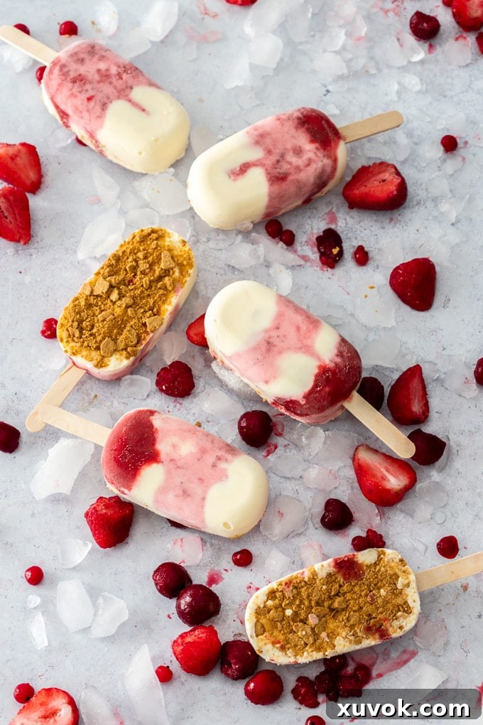 Flatlay of 6 Strawberry Cheesecake Ice Cream Bars on a concrete background surrounded by ice and berries, showcasing the vibrant colors and appealing texture.