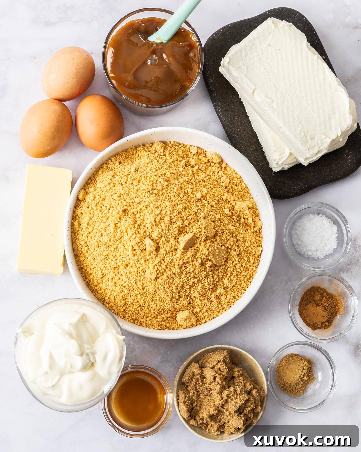 All the fresh ingredients for a baked caramel cheesecake laid out on a clean marble surface, ready for preparation.