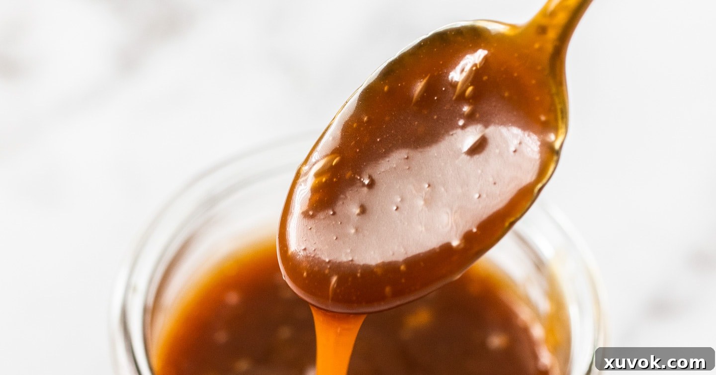A spoon coated with rich, golden caramel sauce, held above a glass jar filled with more homemade caramel.