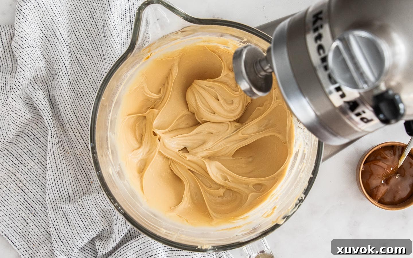 Cream cheese, sugar, and caramel sauce perfectly blended in a stand mixer bowl, forming a smooth, light brown mixture.