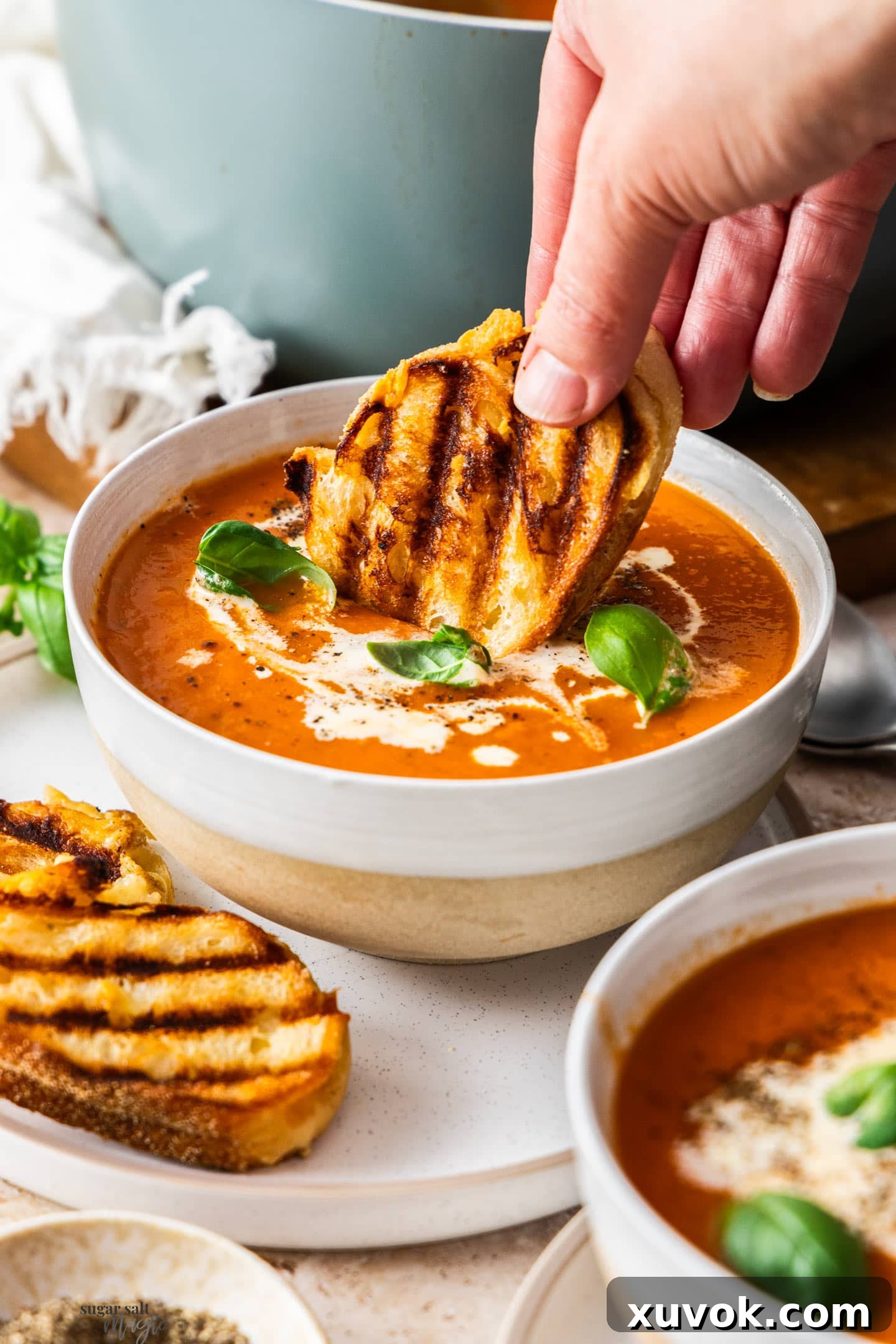 A hand gracefully dipping a crispy mini grilled cheese sandwich into a vibrant bowl of roasted garlic tomato soup.
