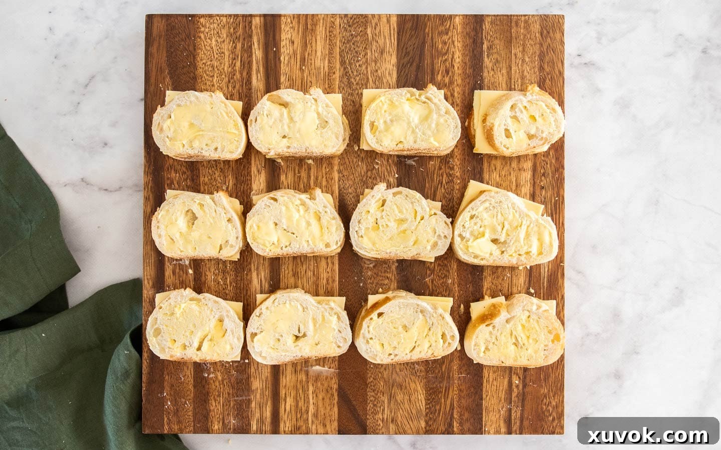 A dozen mini grilled cheese sandwiches, fully assembled and ready for grilling, arranged on a wooden board.