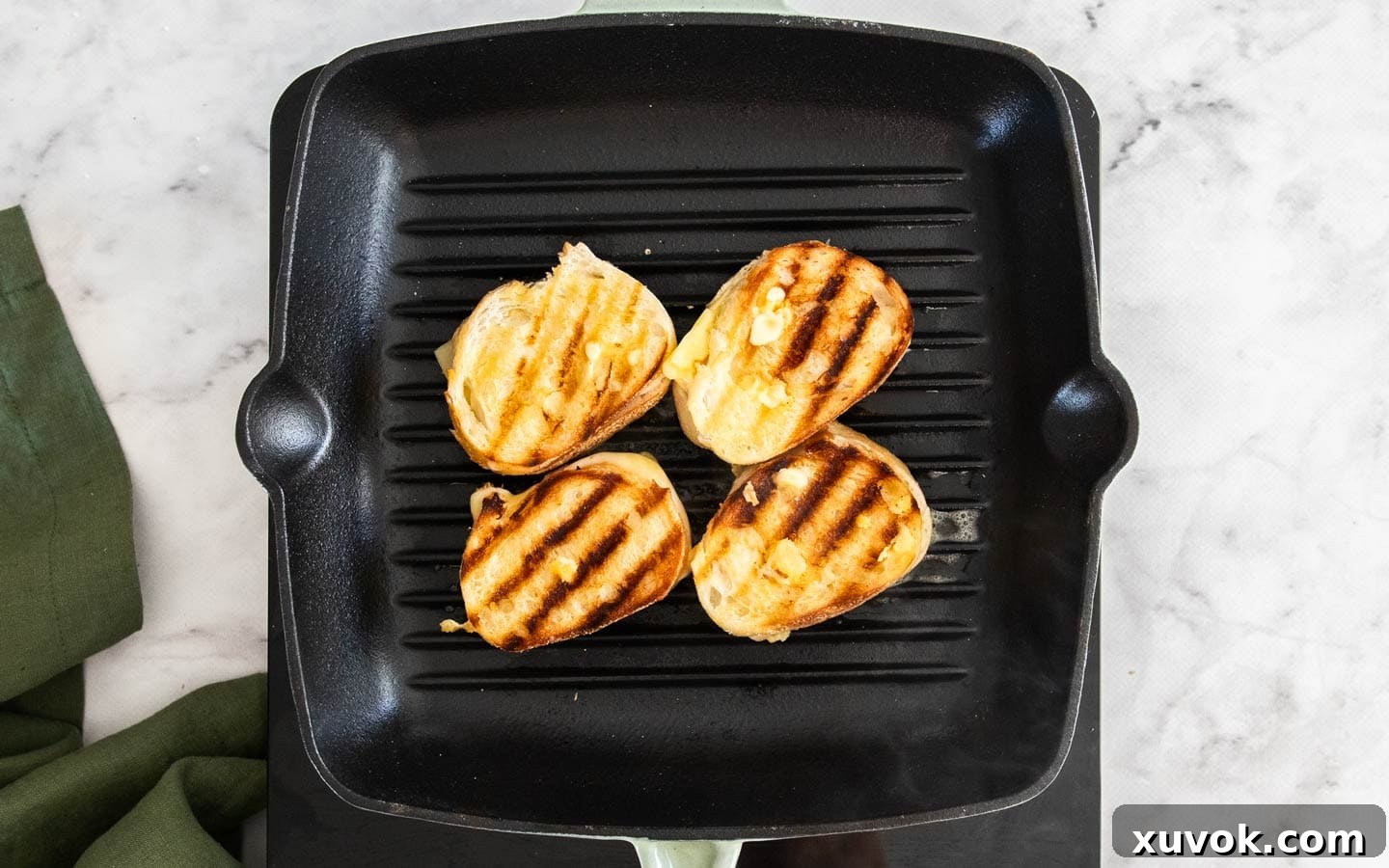 Mini grilled cheese sandwiches cooking on a hot grill pan, showing appealing char marks on their golden-brown surface.