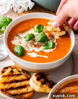 A hand dipping a piece of mini grilled cheese into roasted garlic tomato soup.