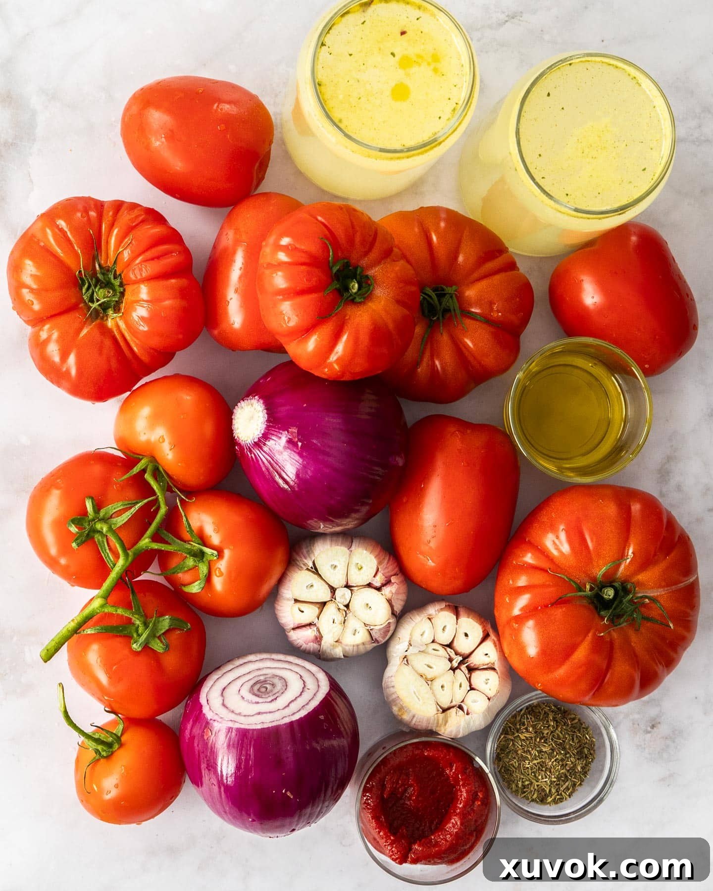 A beautiful display of fresh, ripe ingredients for roasted garlic tomato soup: various tomatoes, red onions, garlic bulbs, and olive oil.