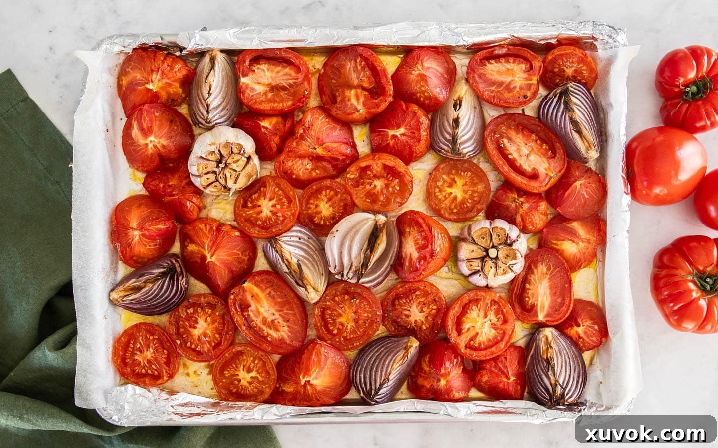 The roasted vegetables on the baking sheet after cooking, showing tender, caramelized tomatoes, onions, and garlic.