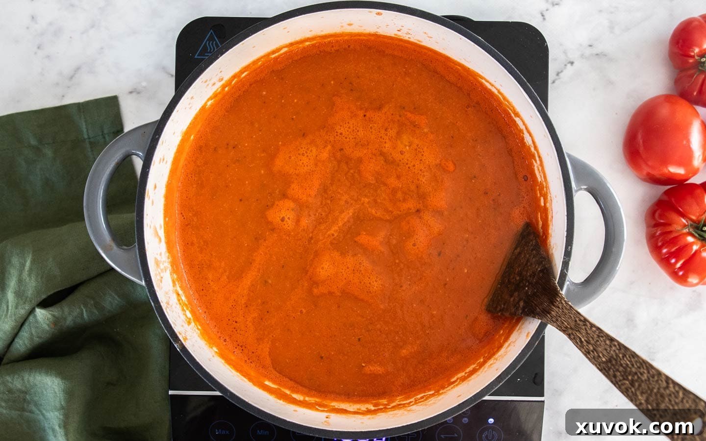 The roasted garlic tomato soup gently simmering in a red Dutch oven, steam rising from its surface.