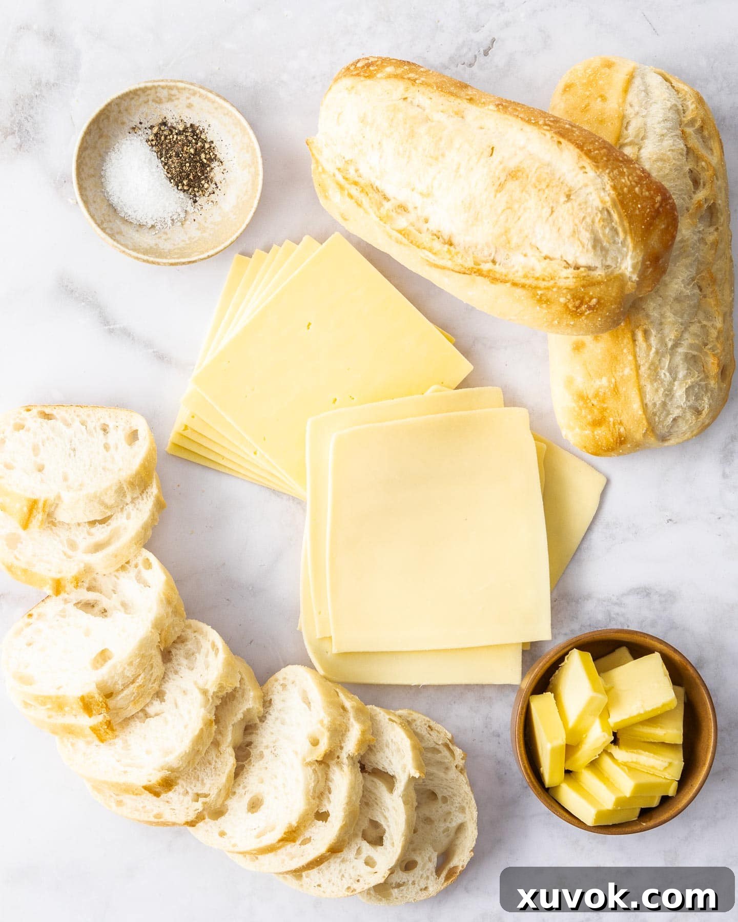 Ingredients for mini grilled cheese sandwiches, including sliced baguette, butter, and two types of cheese.