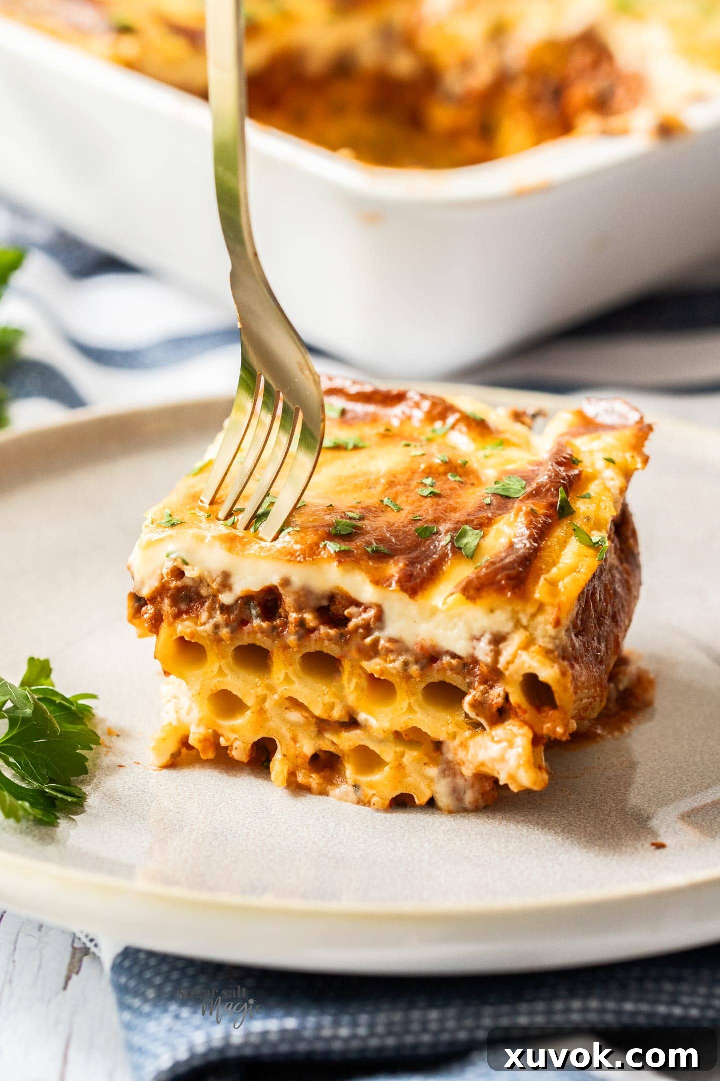 A close-up of a slice of Pastitsio on a plate, with a fork digging into the layers, emphasizing its comforting texture.