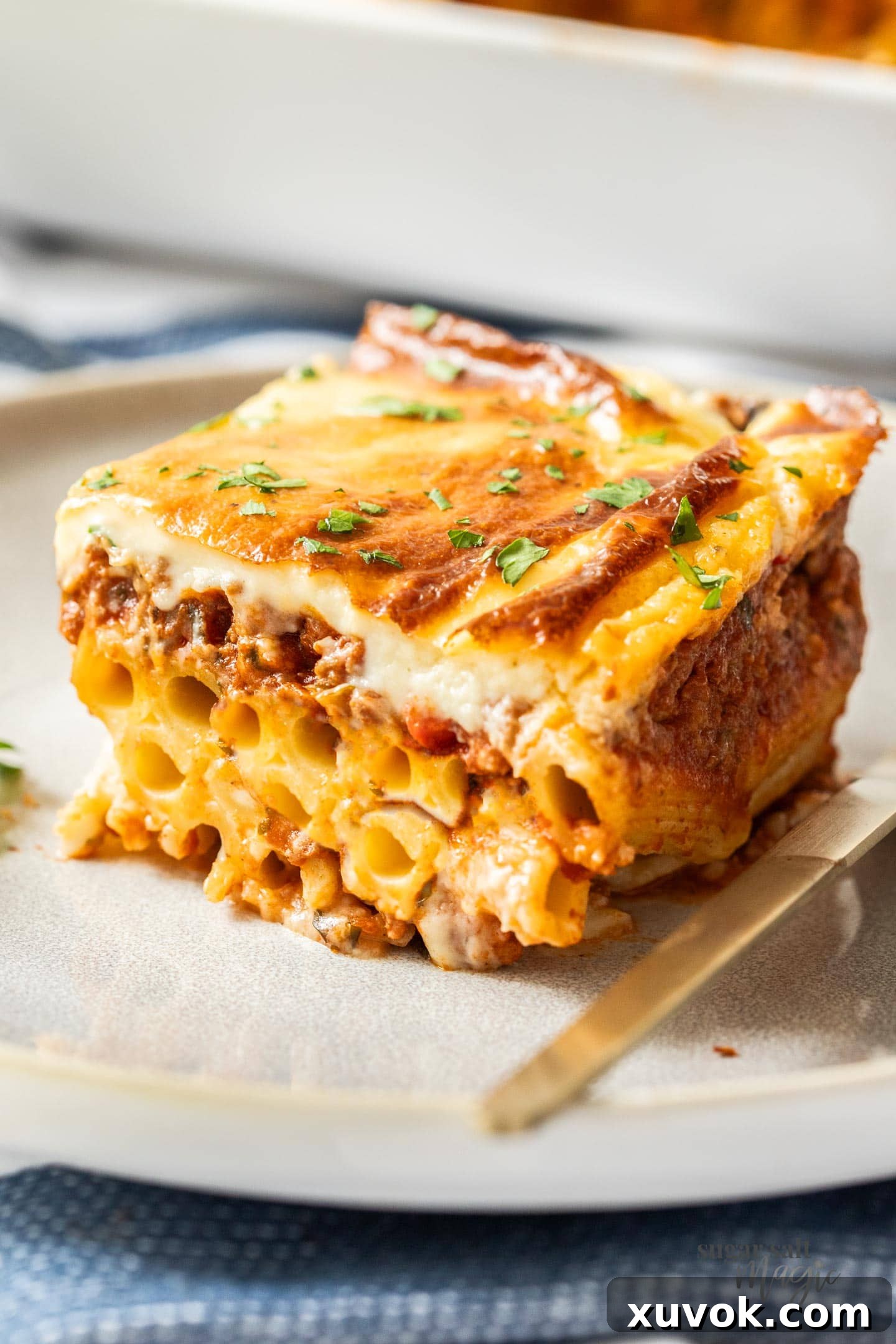 A perfectly cut slice of Pastitsio on a white plate, showcasing its distinct layers of pasta, meat sauce, and creamy béchamel topping.