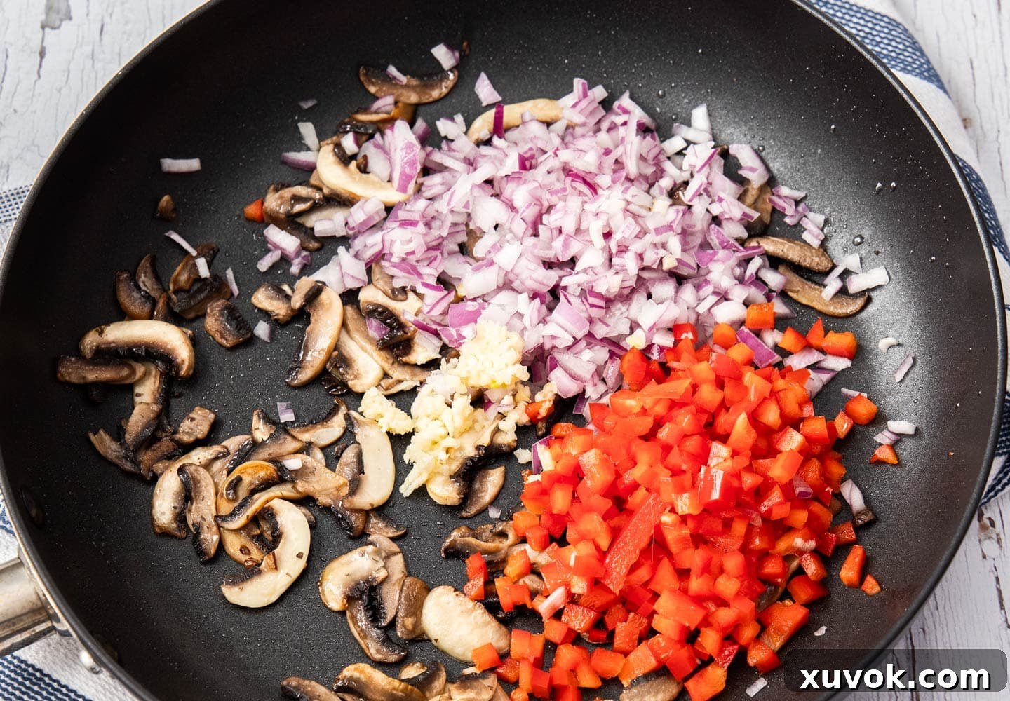 Vegetables including mushrooms, onions, garlic, and capsicum cooking in a frying pan, beginning to soften and gain color.
