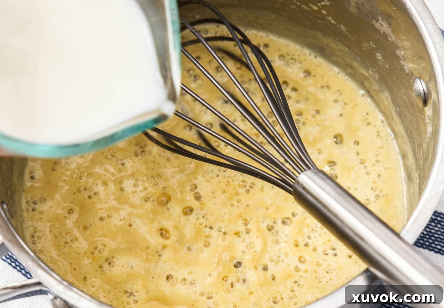 Adding milk to the flour and butter roux in a pan, whisking to combine.