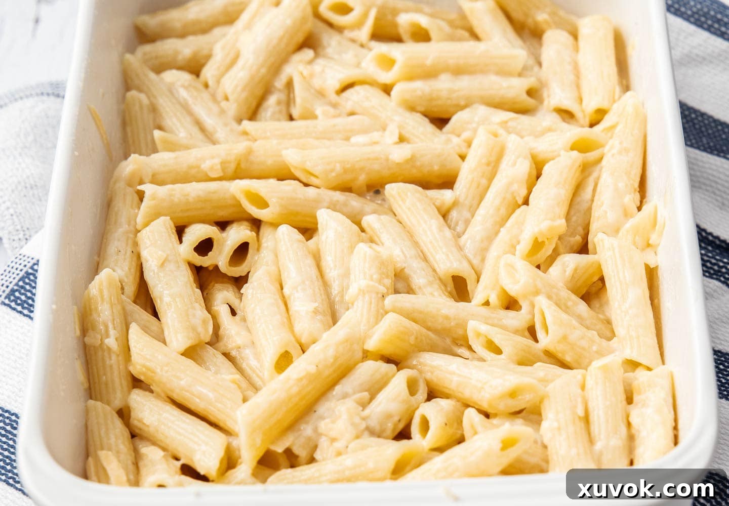 The pasta layer pressed into a baking dish, coated in béchamel and cheese, ready for the next layer.