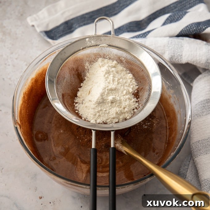 A sieve with flour and cocoa sitting over a glass bowl of chocolate batter