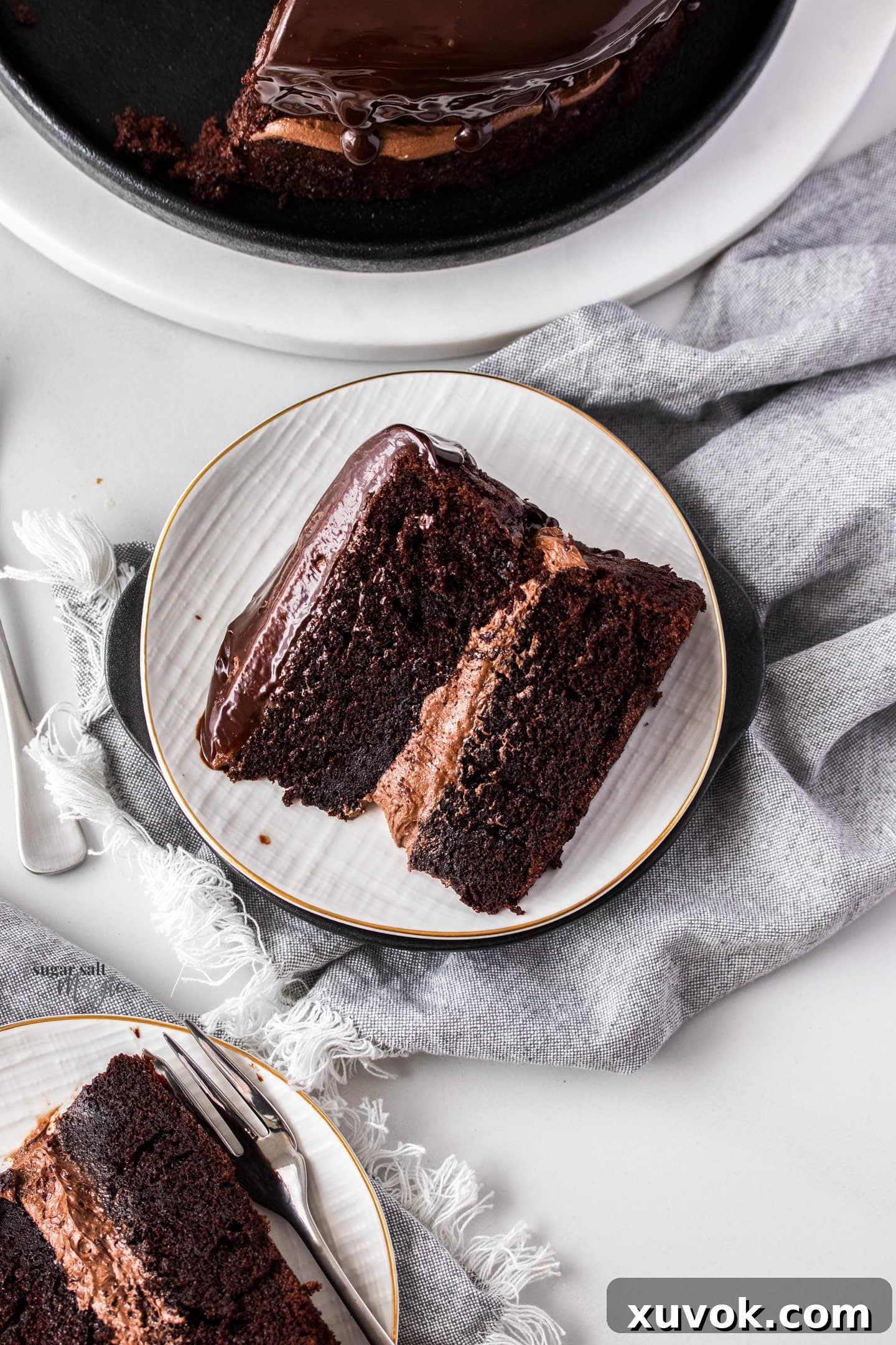 A close-up, top-down view of a single slice of Black Magic Cake, showcasing its dense, moist crumb and the generous layers of chocolate ganache frosting. It sits on a delicate white dessert plate, ready to be savored.