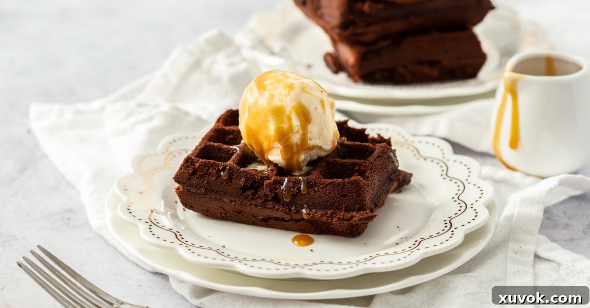 A generous serving of waffle brownies, freshly cooked and perfectly golden, topped with creamy vanilla ice cream and glistening caramel sauce. Two waffle brownies are on the white plate in the foreground, with more blurred in the background, creating an inviting scene.