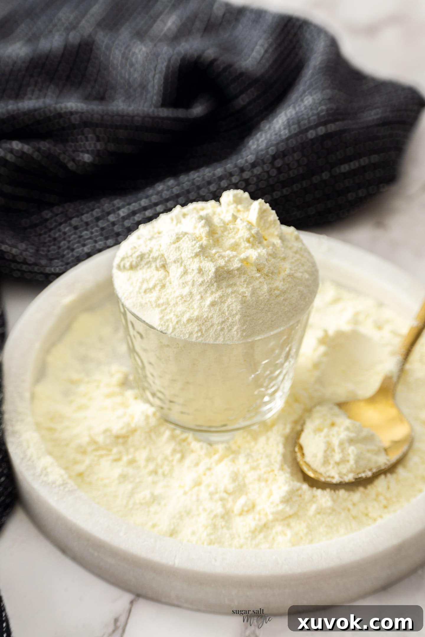 A glass overflowing with homemade custard powder on a marble plate, highlighting its fine texture and inviting color.