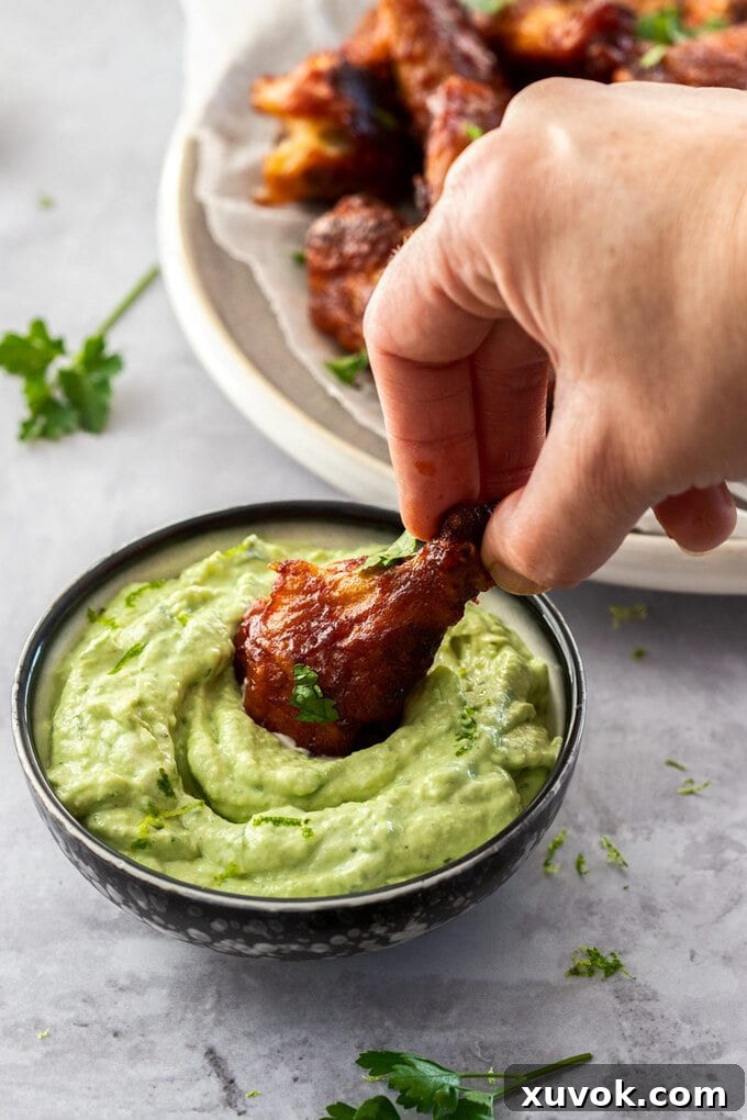A perfectly cooked chicken wing being dipped into a creamy, vibrant green avocado cream sauce, highlighting its rich texture and appealing color, perfect for adding zest to any meal.