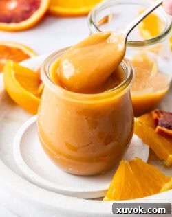 A spoon taking smooth orange curd out of a glass jar, demonstrating its creamy texture.