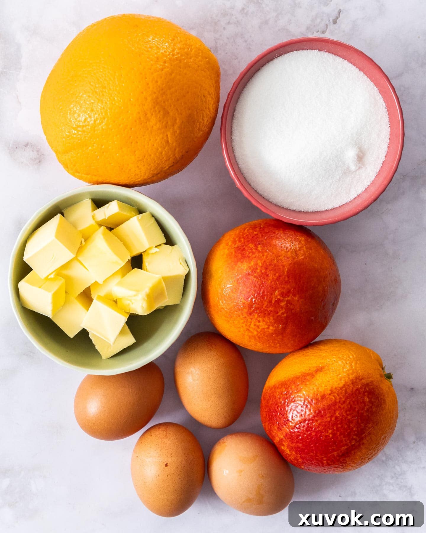 A simple array of ingredients for making orange curd, including fresh oranges, eggs, sugar, and butter.