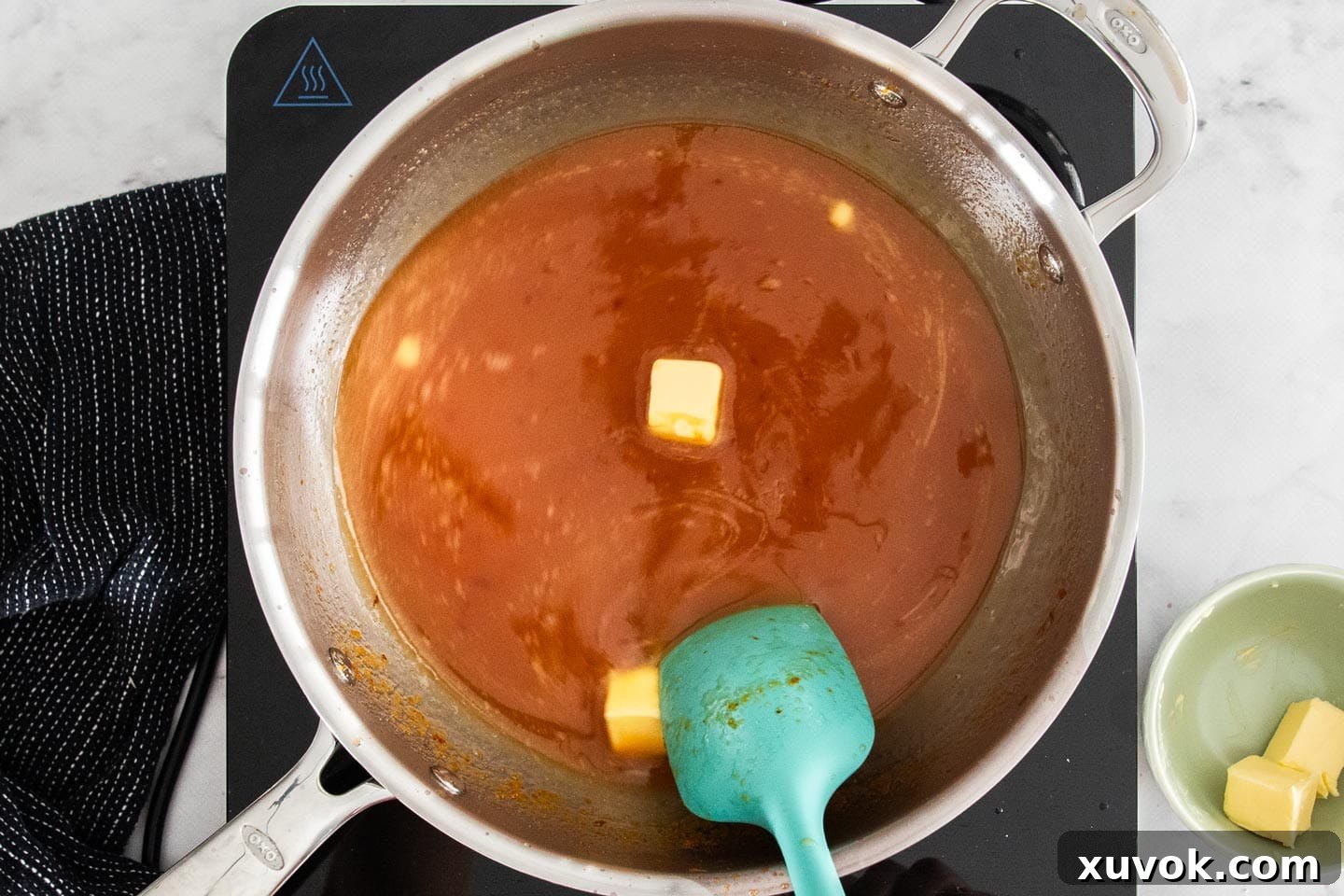 Cubed butter being added incrementally to the simmering orange curd mixture in a pan.
