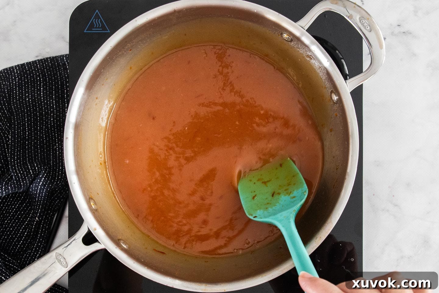 The blood orange curd mixture thickening in a saucepan, being stirred with a whisk.