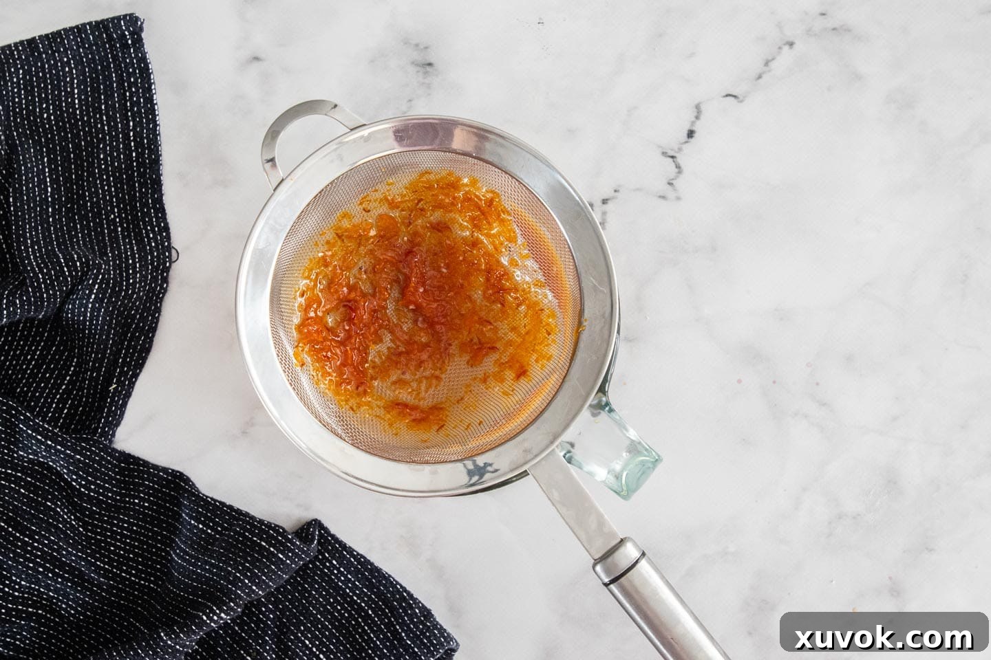 Warm orange curd being strained through a fine-mesh sieve into a bowl for a smooth texture.