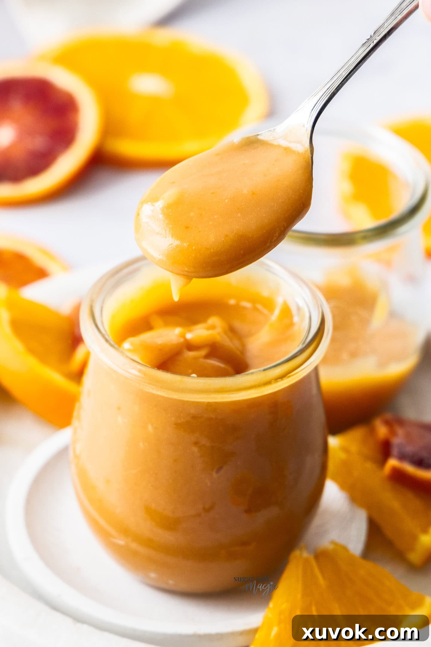 A spoon scooping creamy, smooth orange curd from a glass jar, showing its perfect consistency.