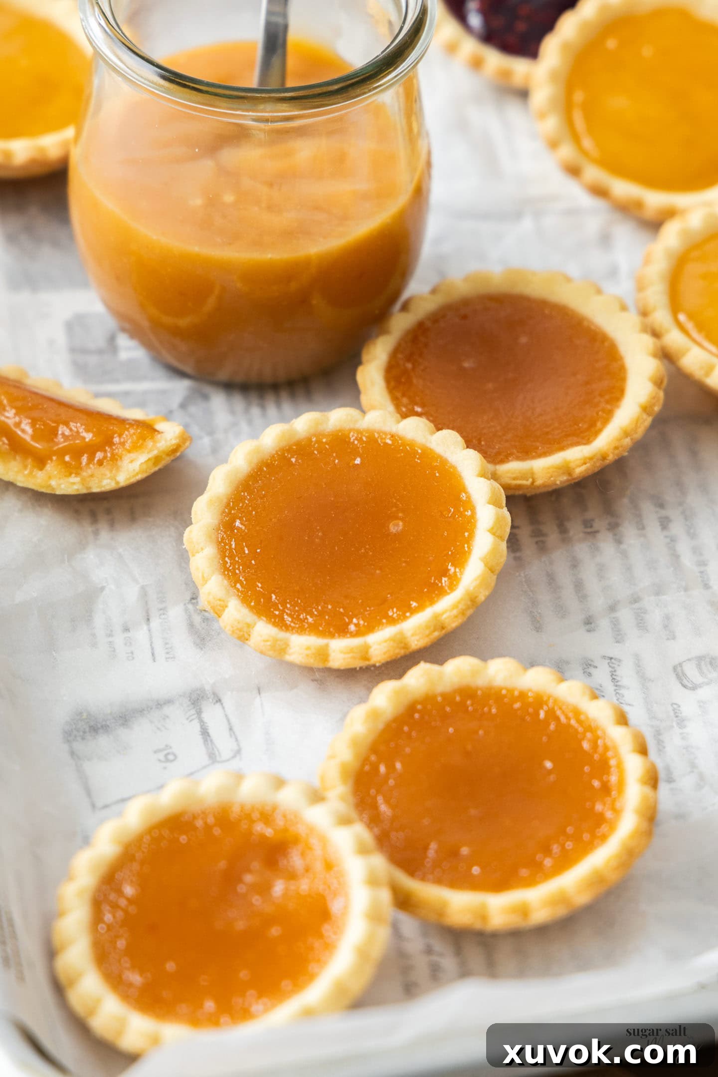 Small, decorative tarts filled with golden-orange curd, garnished with fresh berries.