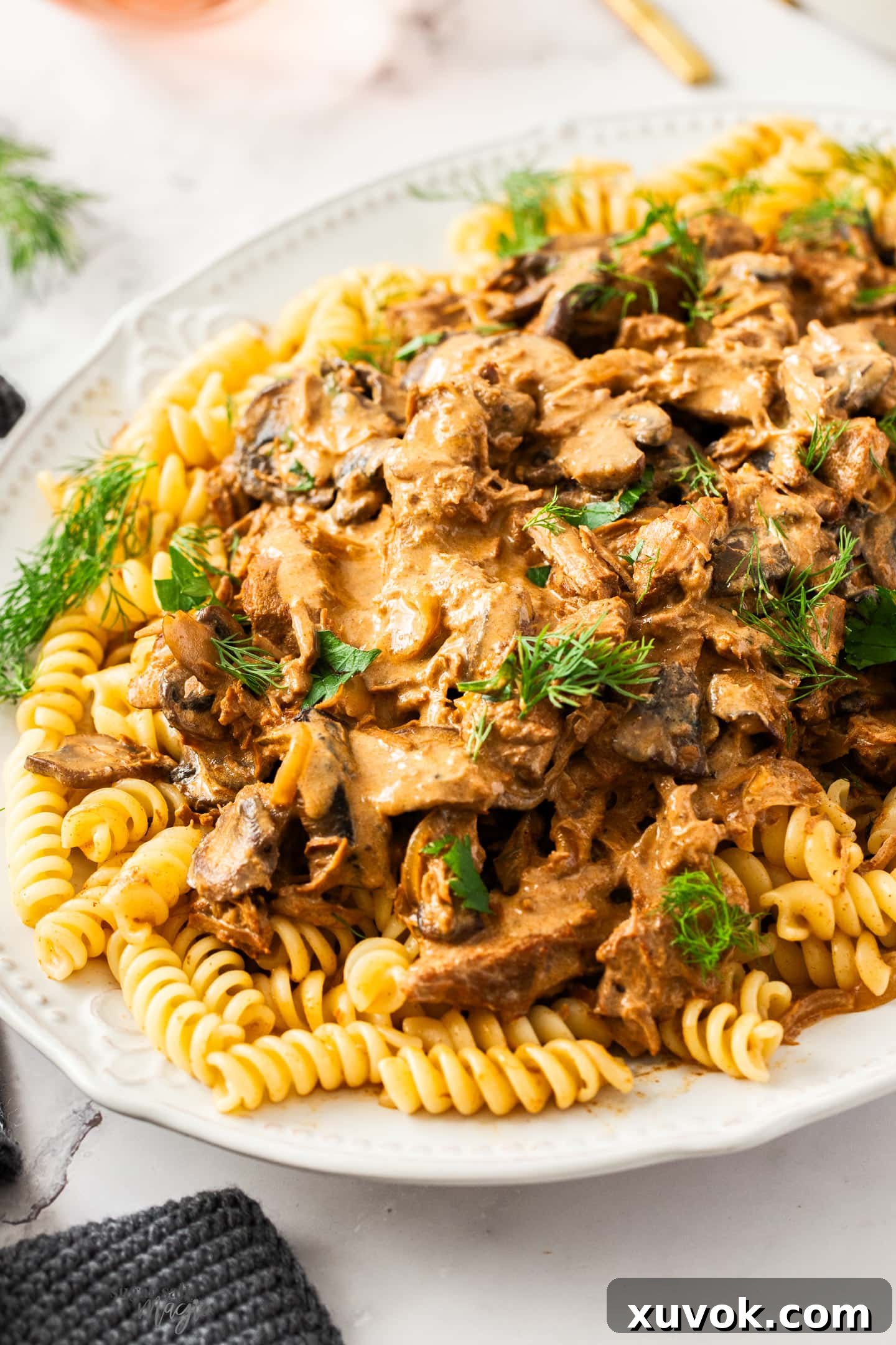 Closeup of slow cooker beef stroganoff on pasta on a platter, garnished with fresh herbs.