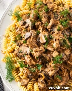 A white dish filled with pasta and slow cooker beef stroganoff, garnished.