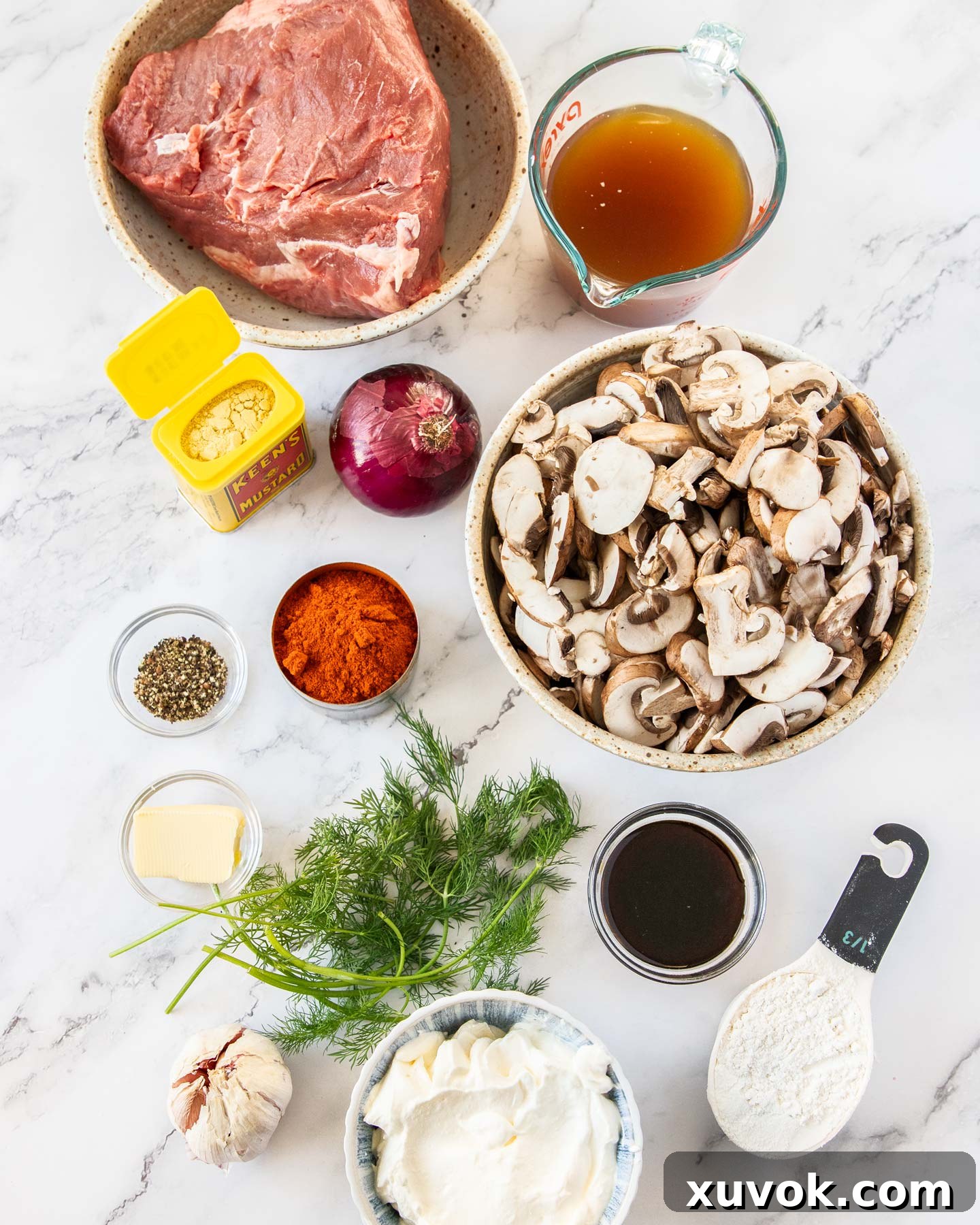 Ingredients for beef stroganoff laid out on a marble surface, including beef, mushrooms, herbs, and spices.