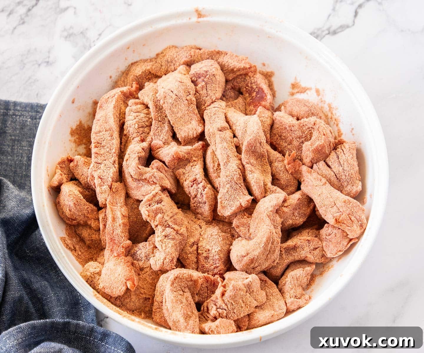 Beef strips coated in flour and spices in a bowl, ready for browning.