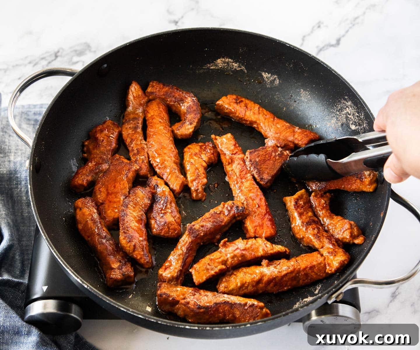 Searing the beef strips in a pan to create a rich crust.