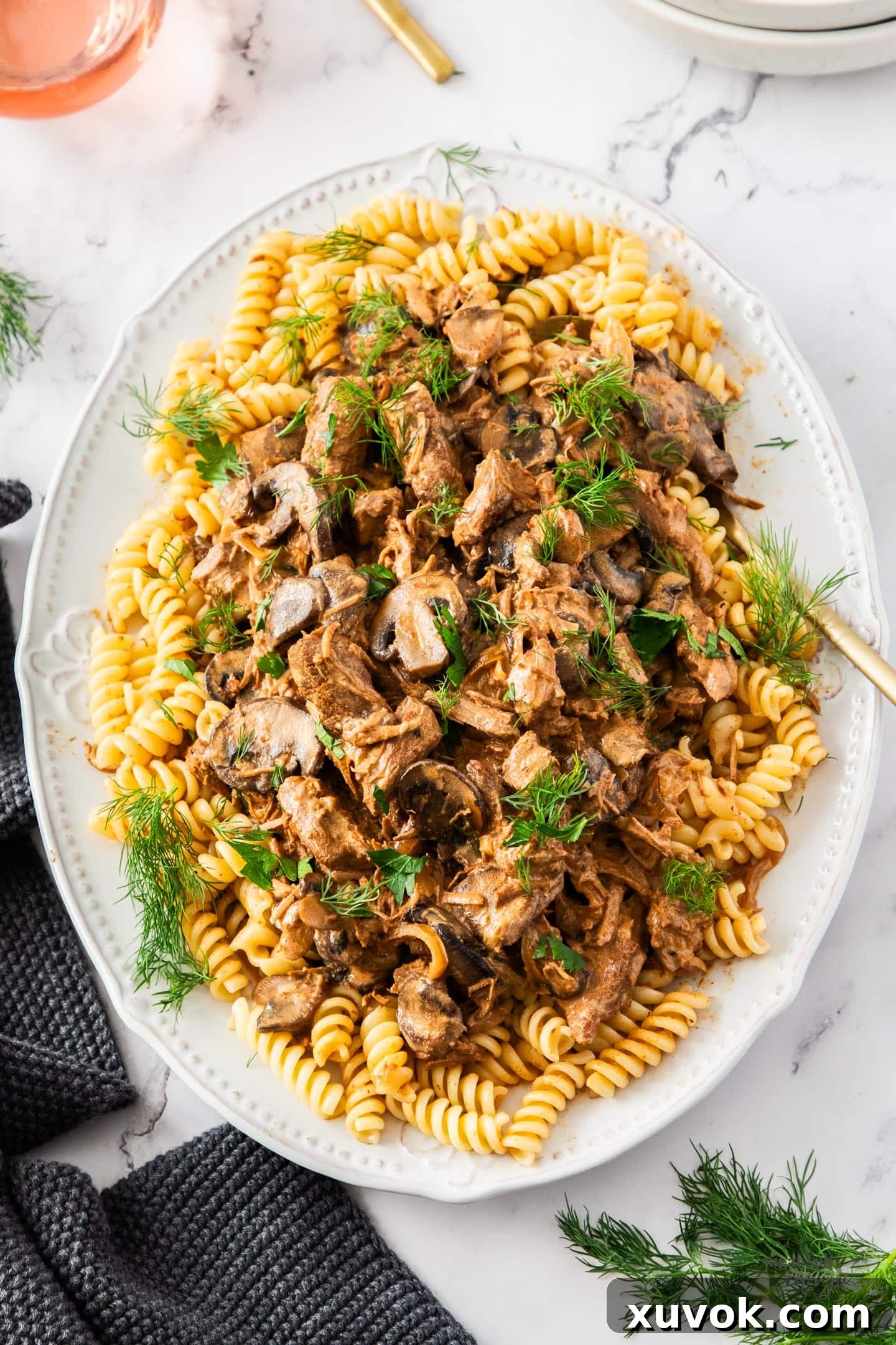 Top down view of slow cooker beef stroganoff served over pasta on a platter, garnished with fresh herbs.