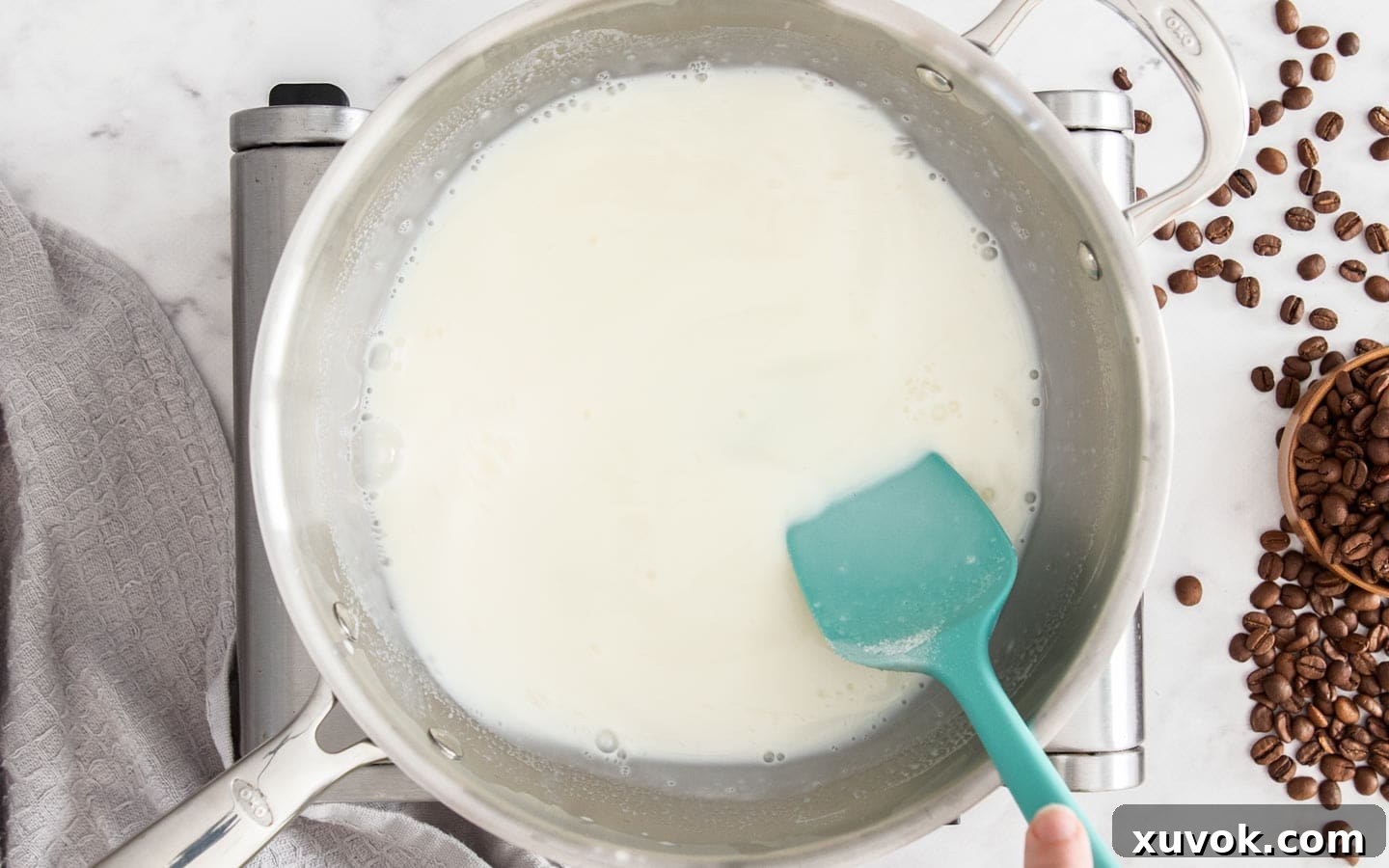 A silicone spatula stirring bloomed gelatin and sugar into warm milk in a saucepan.