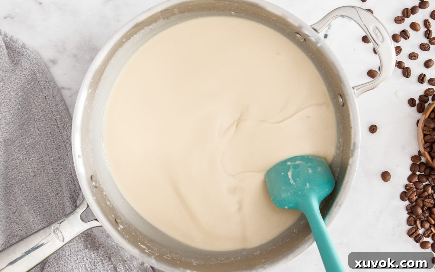 A hand stirring rich coffee into the creamy milk mixture in a saucepan.